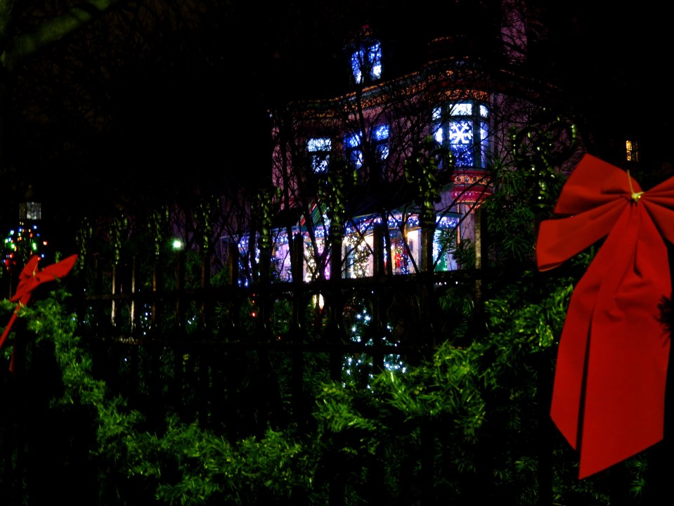 Garland and red bow drape the wrought iron fence surrounding the house.
