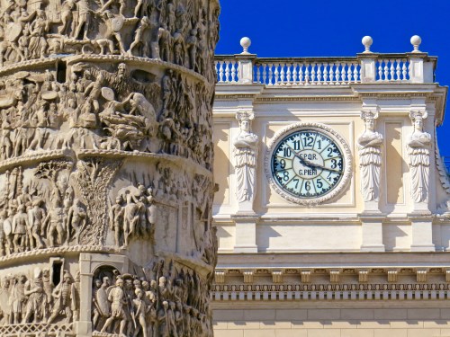Close up detail of the Column of Marcus Aurelius with the clock of the Palazzo Wedekind in the background.